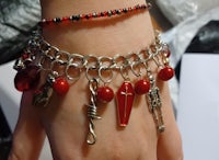 a woman's hand is holding a bracelet with red beads and charms